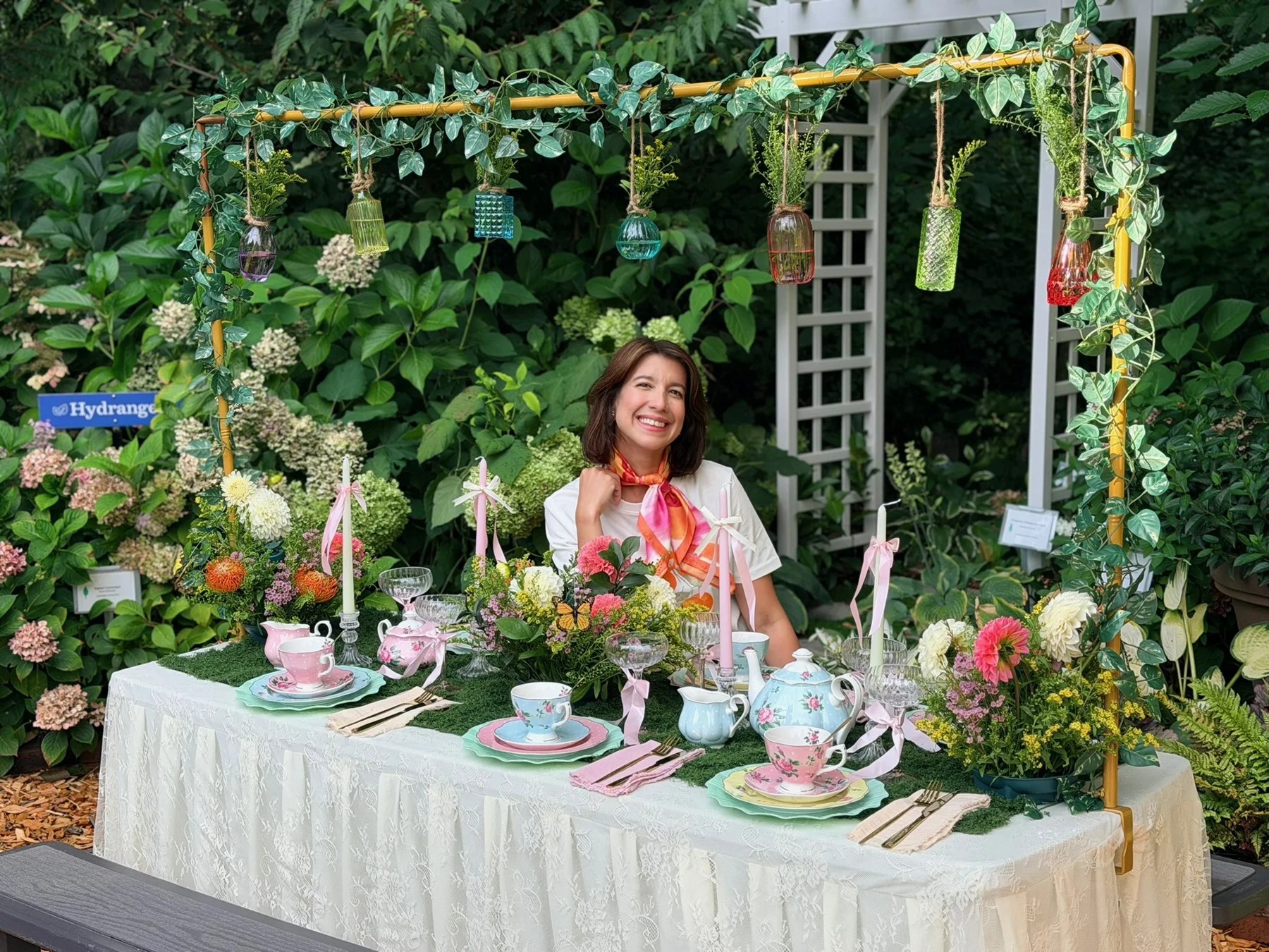 A guest behind the garden tea table with pastel china and hanging glass vases